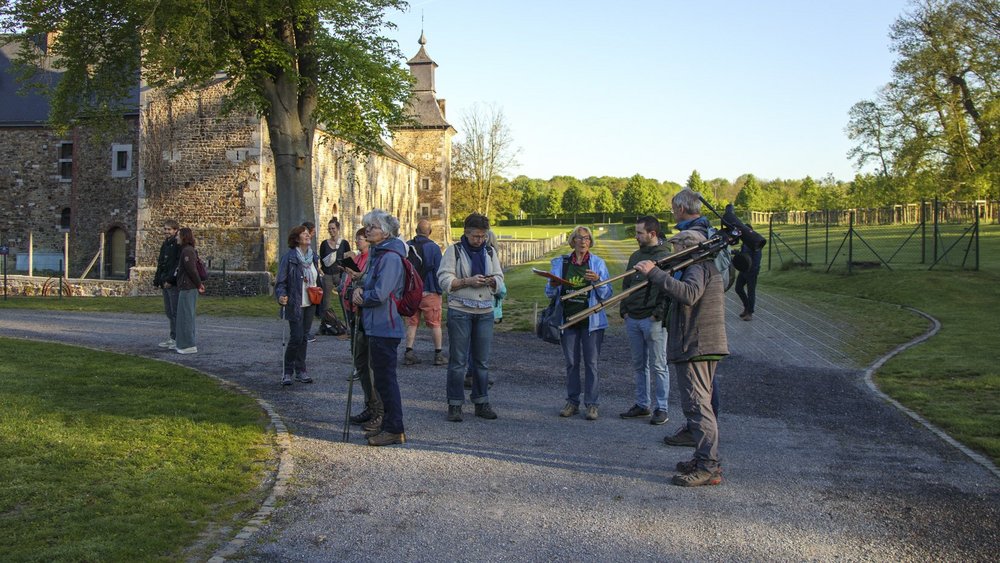 Photo des participants, le volontaire Natagora Albert porte une longue-vue ornithologique et la volontaire Solange donne des explications. Certains participants regardent le ciel ou les arbres en souriant.
