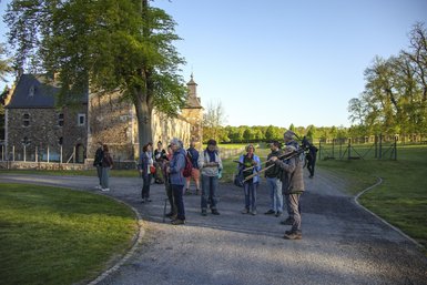 Photo des participants, le volontaire Natagora Albert porte une longue-vue ornithologique et la volontaire Solange donne des explications. Certains participants regardent le ciel ou les arbres en souriant.