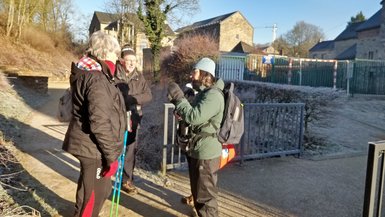 Une personne (Sigrid) donne des explications à trois autres personnes sur un petit chemin de village. Ils sont chaudement habillés, on voit du gel au sol malgré l'ensoleillement.